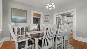 Uma sala de jantar com mesa de madeira e cadeiras brancas, um candelabro e um quadro na parede.