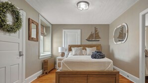 Quarto com cama de madeira, mesa de cabeceira, luminária, radiador, porta e espelho fixado na parede.