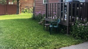 En stuga av trä med en inhägnad trädgård, ett litet bord och en stol.