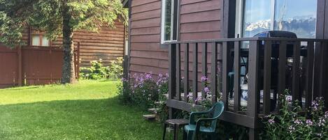 A wooden cabin with a fenced yard, a small table, and a chair.