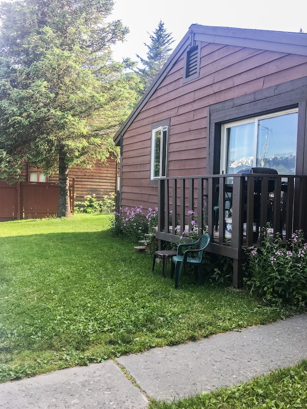 A wooden cabin with a fenced yard, a small table, and a chair.
