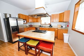 A modern kitchen with a stainless steel refrigerator, wooden cabinets, a central island with stools, and a microwave.