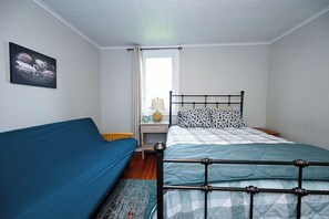 A single bed with a metal frame, a bedside table with a lamp, a wall-mounted picture, and a window with curtains.