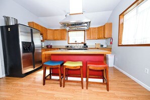 A kitchen with a stainless steel refrigerator, wooden cabinets, a central island with stools, and a window above the sink.