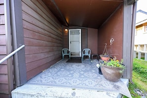A porch with a patterned rug, two chairs, a potted plant, and a door.