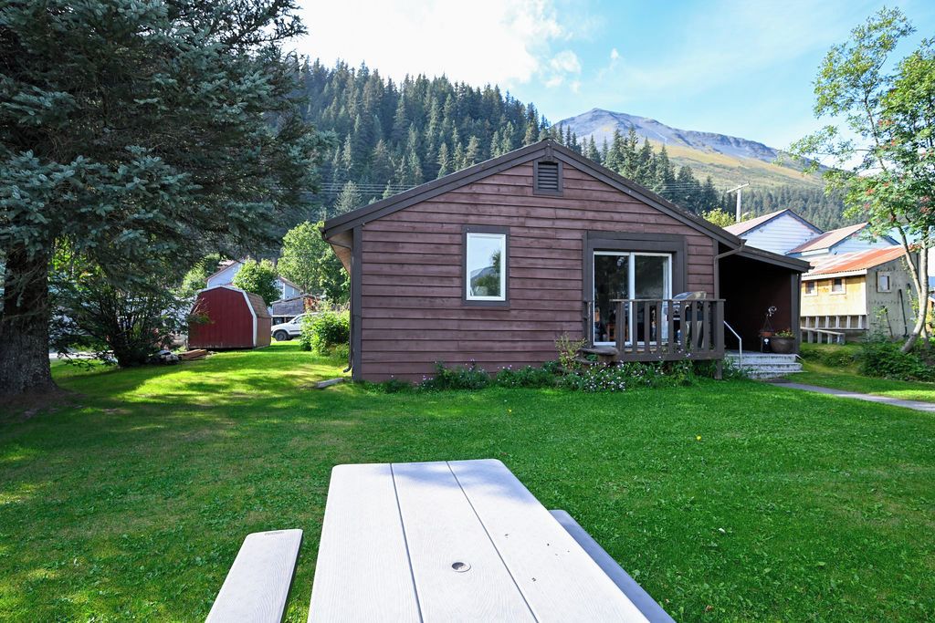 Una baita di legno con veranda, tavolo da picnic e montagne sullo sfondo.