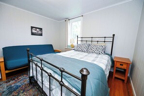 A bedroom with a bed, a blue sofa, a bedside table, and a window.
