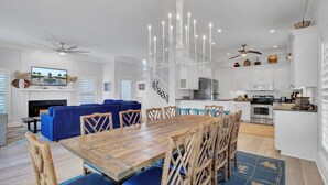 A spacious living room with a wooden dining table, blue sofas, and a staircase leading to the upper floor. - Award-Winning Resort Amenities | Grand Pavilion 31 by Wild Dunes (Isle of Palms)