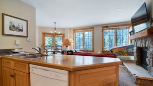 A spacious kitchen with wooden cabinets, a dishwasher, and a large island. There is a dining area with a table and chairs, and a fireplace with a stone surround.