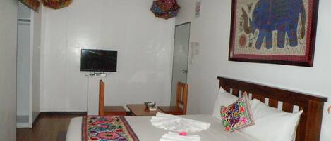 Habitación de hotel con cama, televisión, cabecero de madera, obra de arte colorida y un adorno colgante en la pared.