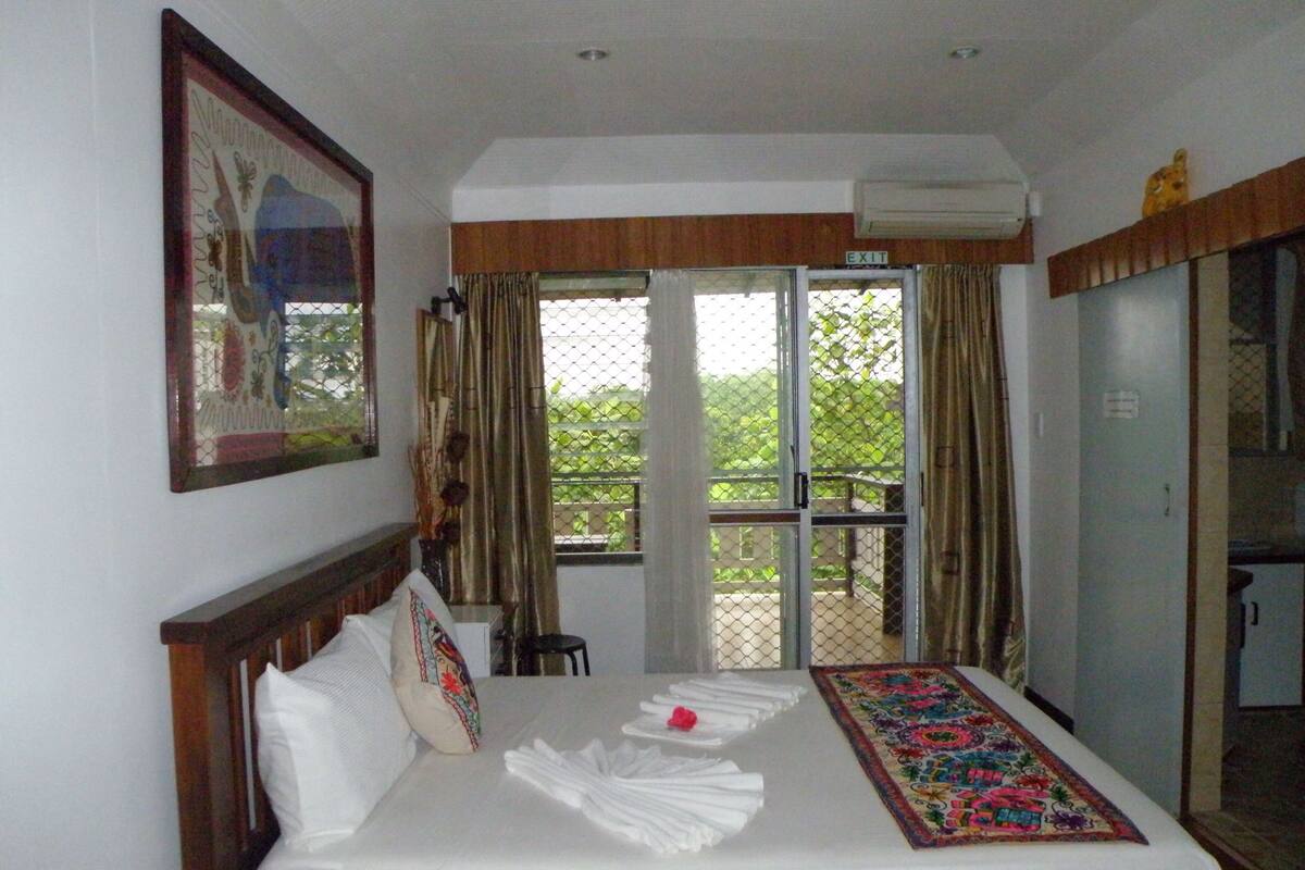 A hotel room with a bed, a window with curtains, a door, and a framed picture on the wall.