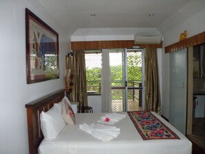 A hotel room with a bed, a window with curtains, a door, and a framed picture on the wall. - Tagimoucia House Hotel (Suva)