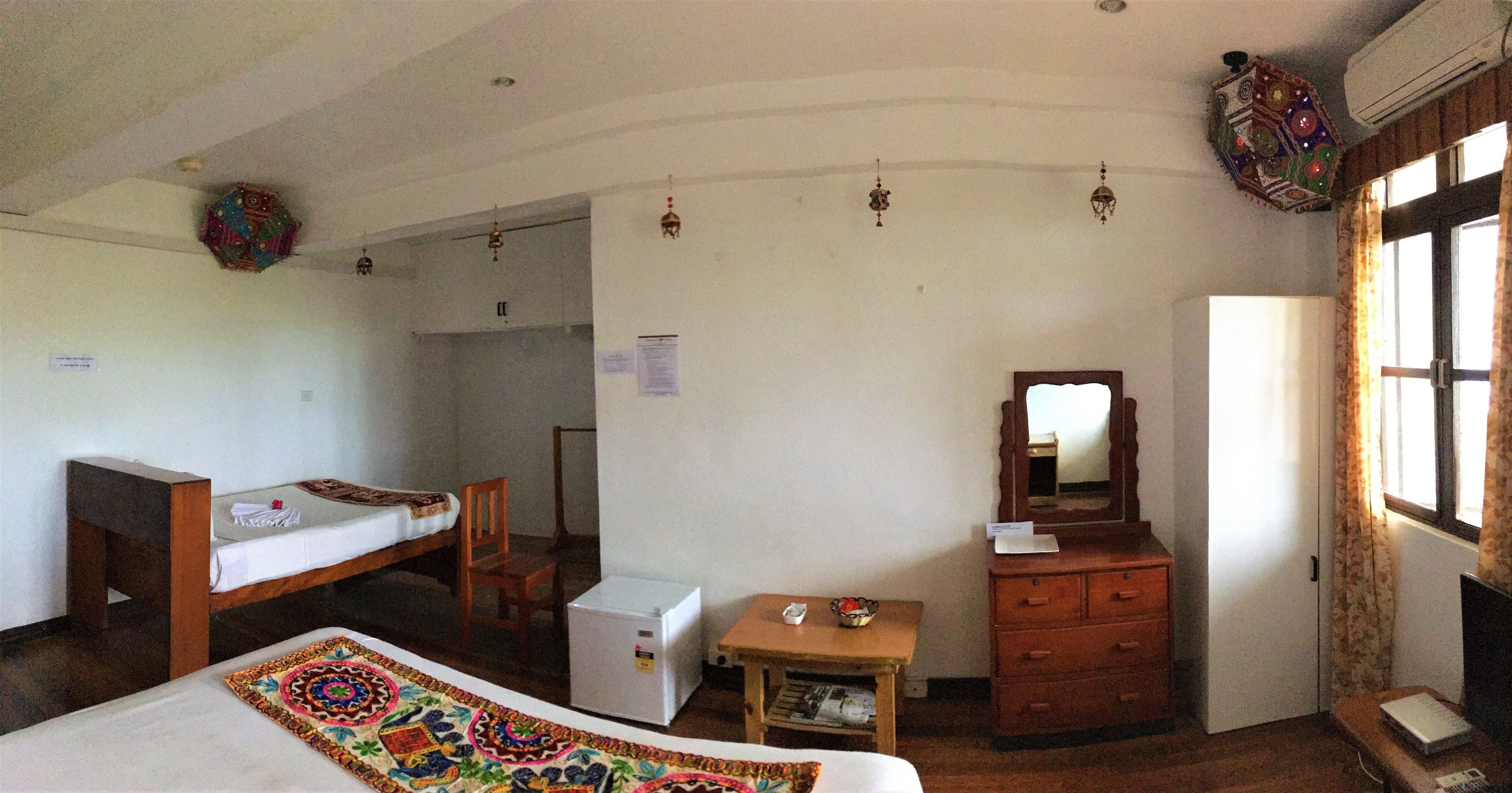 A room with a bed, a desk, a dresser, a small table, and a refrigerator.