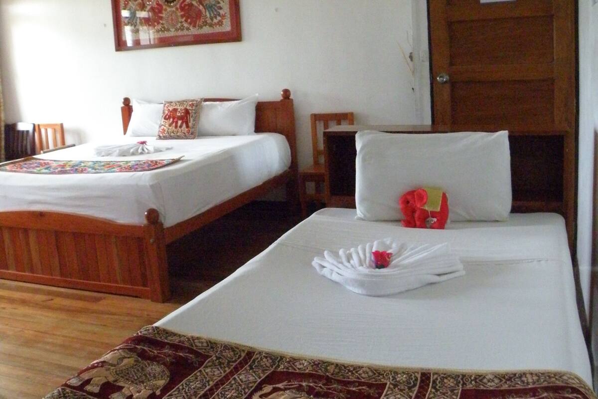 A hotel room with two single beds, each with a wooden headboard and white bedding. There is a wooden nightstand with a lamp, a framed picture on the wall, and a door with a sign.