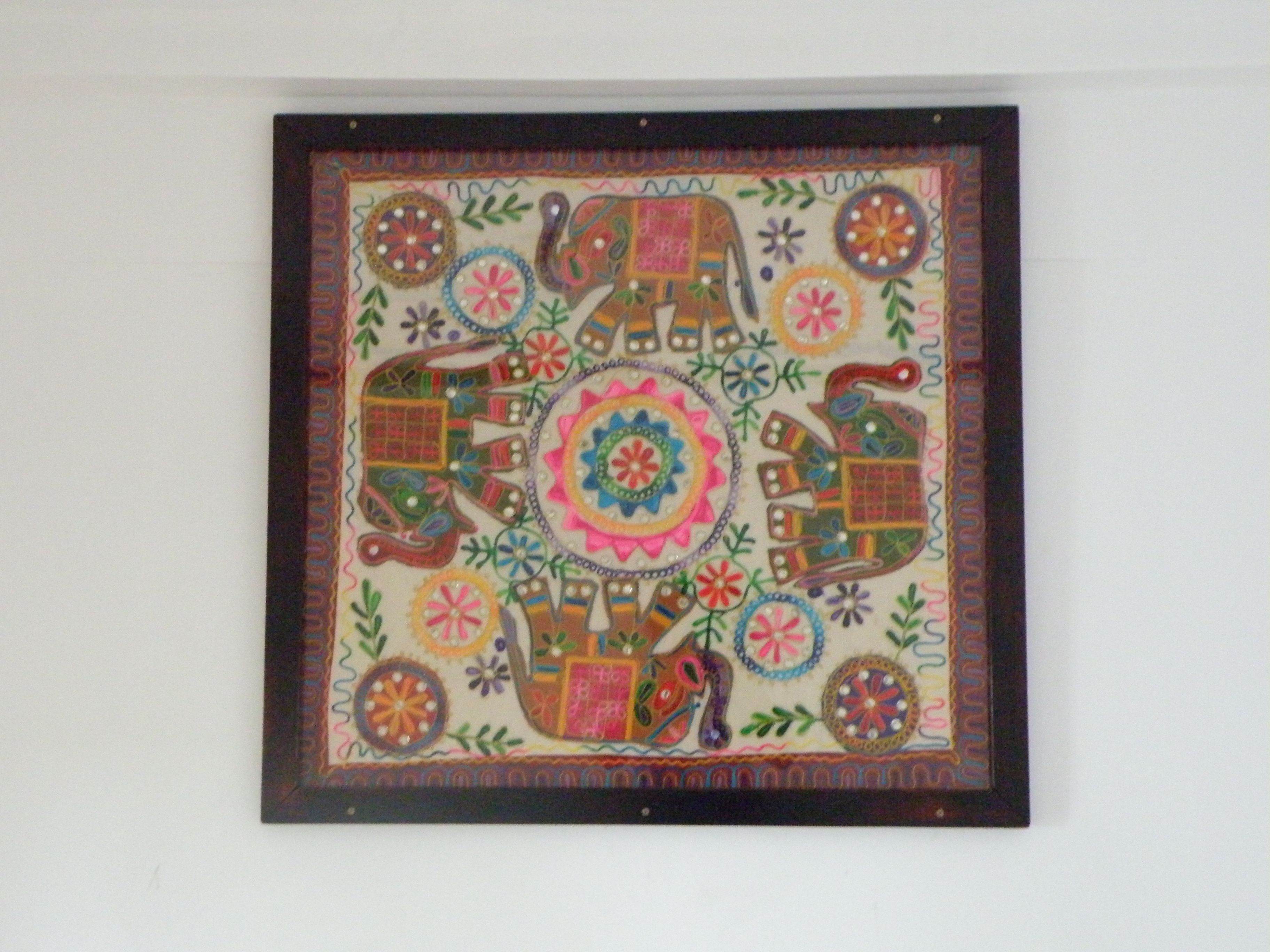 Una obra de arte textil enmarcada, con diseños intrincados y un motivo circular central.