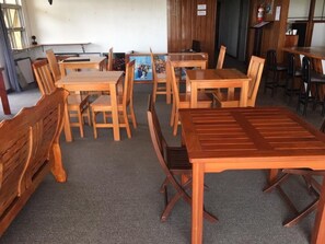 A dining area with wooden tables and chairs, a fire extinguisher on the wall, and a view of the outside through a window. - Tagimoucia House Hotel (Suva)