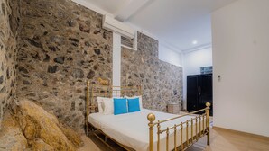 A bedroom with a stone wall, a bed with a gold frame, and a wooden floor. - Meadow Villa - Galle (Galle)