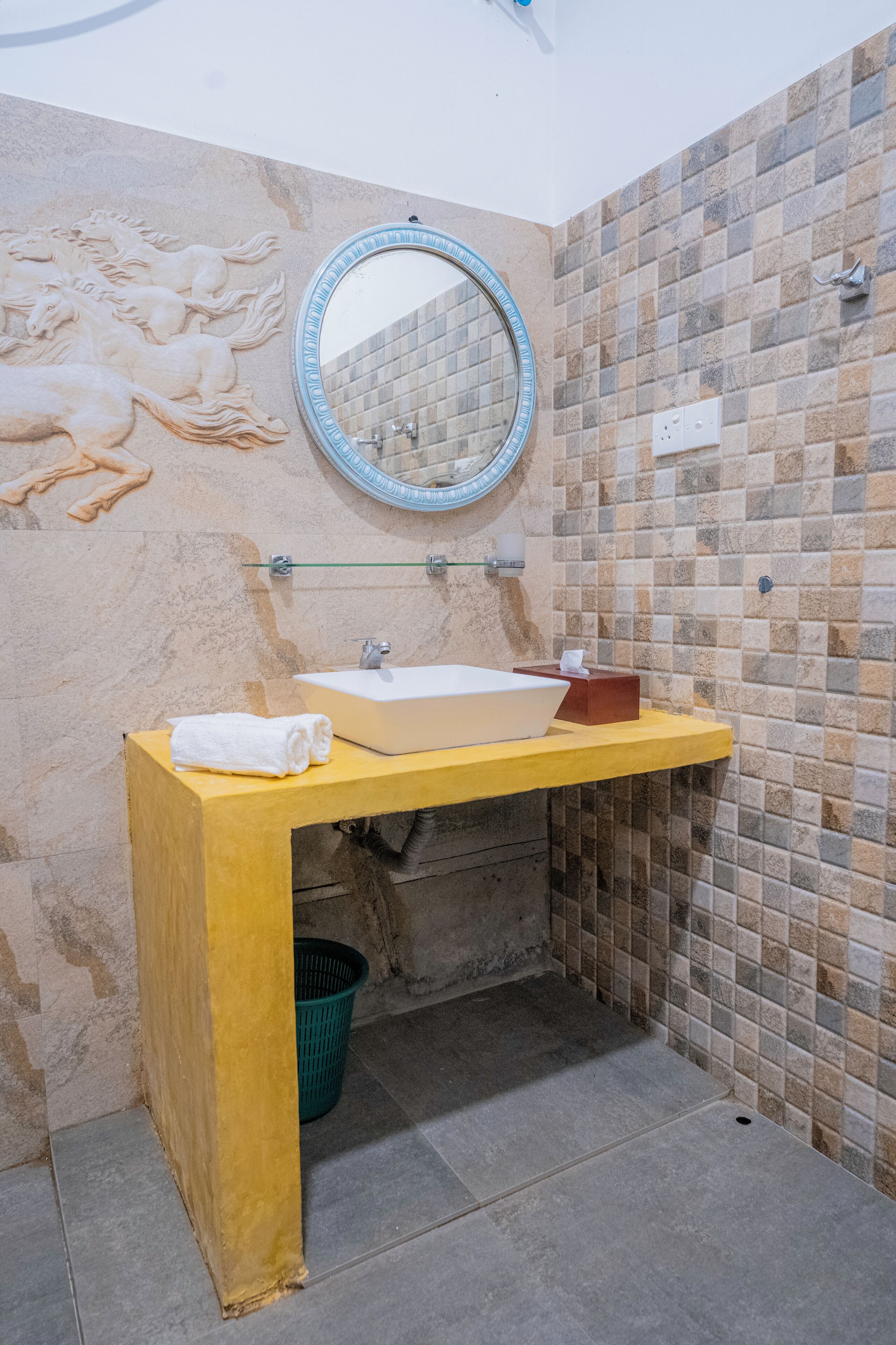 A bathroom with a beige sink, a mirror, and a decorative wall with a mosaic pattern.
