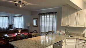 A kitchen with white cabinets, a granite countertop, and a dishwasher. There is a dining area with a table and chairs. - Location Anastasia Island home, Bring your bikes! (St Augustine)