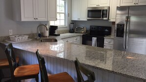 A kitchen with white cabinets, stainless steel appliances, a granite countertop, and wooden bar stools. - Location Anastasia Island home, Bring your bikes! (St Augustine)