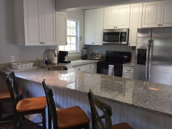 A kitchen with white cabinets, stainless steel appliances, a granite countertop, and wooden bar stools.