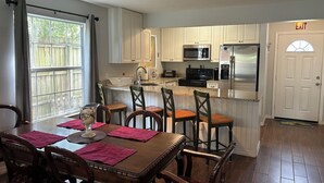 A kitchen with white cabinets, a stainless steel refrigerator, a microwave, and a stove. There is a dining table with chairs and a window with curtains. - Location Anastasia Island home, Bring your bikes! (St Augustine)