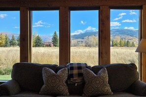 Ein Zimmer mit großem Fenster und Blick auf ein Feld und Berge.