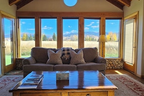 A cozy living room with a large window, a wooden coffee table, and a stone accent wall.