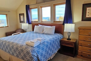 A hotel room with a large bed, two bedside tables, a dresser, and a view of the outdoors through the windows.