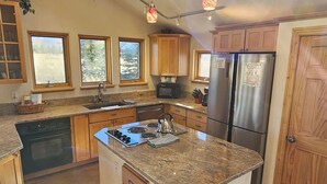 Una cocina con una isla central, horno empotrado, refrigerador de acero inoxidable y armarios de madera.