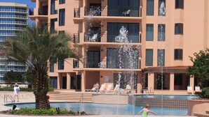 Ein Pool mit mehreren Wasserstrahlen, umgeben von Liegestühlen und einer Palme.