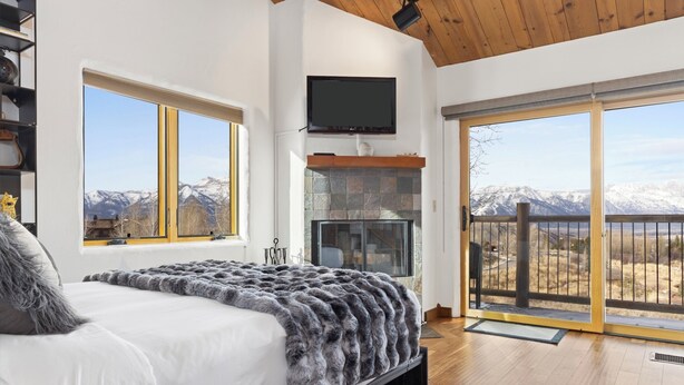 A bedroom with a large bed, a television mounted on the wall, and a view of mountains through the windows. - Outpost: Harvest Dance 3150 - Teton Views (Jackson)