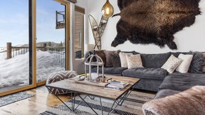 A modern living room with a large window, a grey sofa, a wooden coffee table, and a mounted fur rug. - Outpost: Harvest Dance 3150 - Teton Views (Jackson)