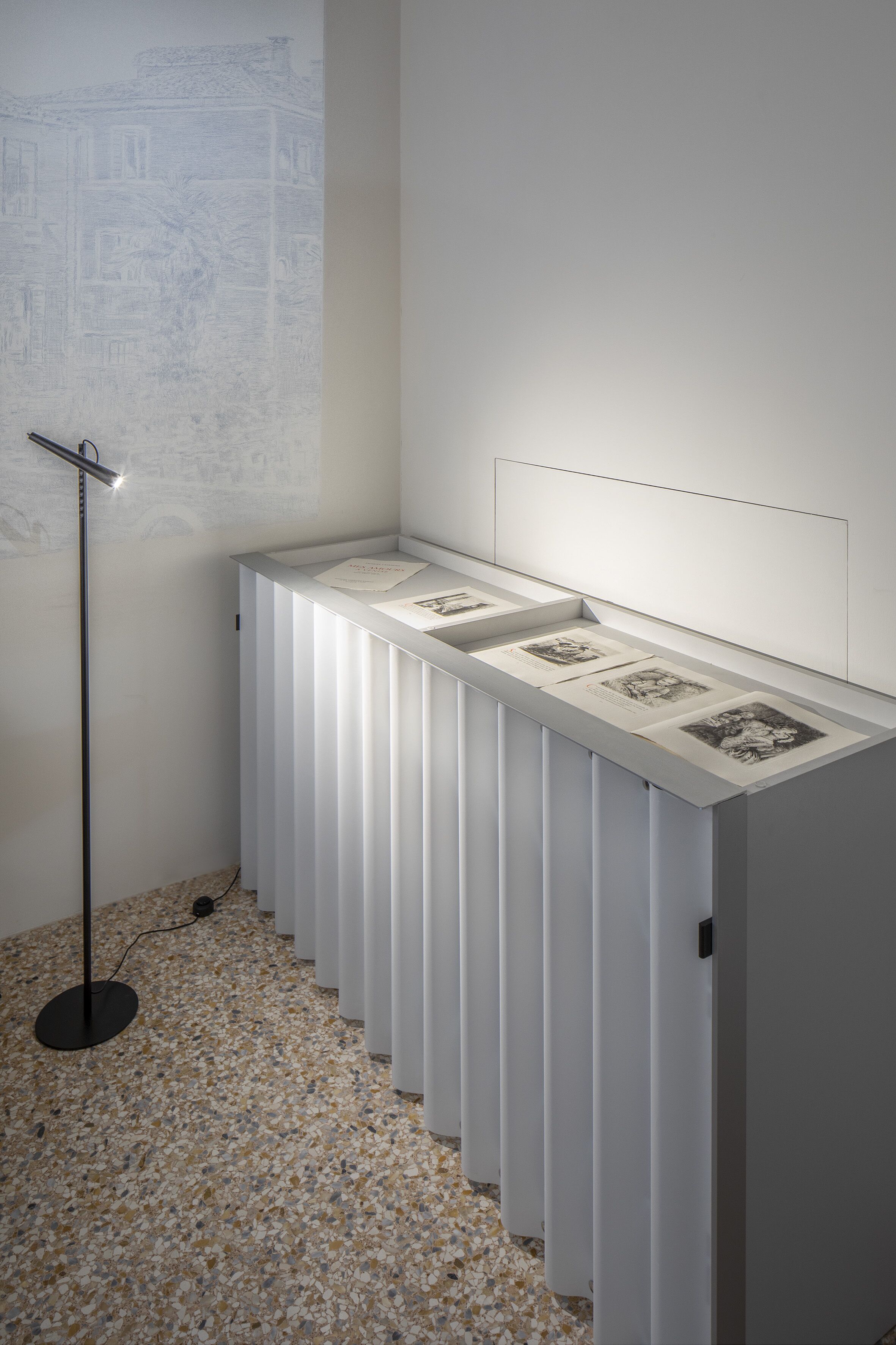Una habitación moderna y minimalista con una pared vertical larga y blanca, y un escaparate de techo a suelo con obras de arte enmarcadas.