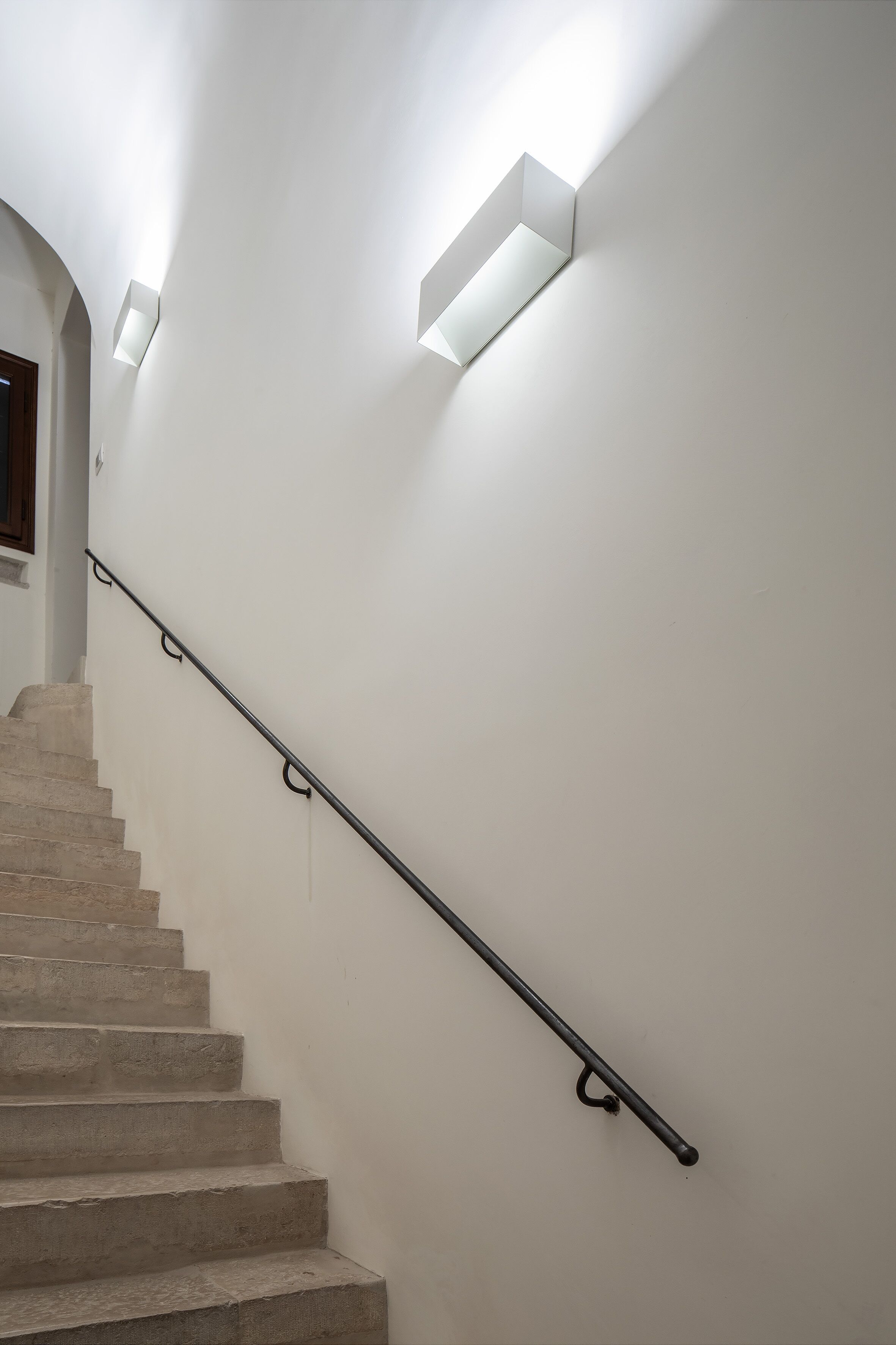Een trap met een leuning en in de muur gemonteerde verlichting.