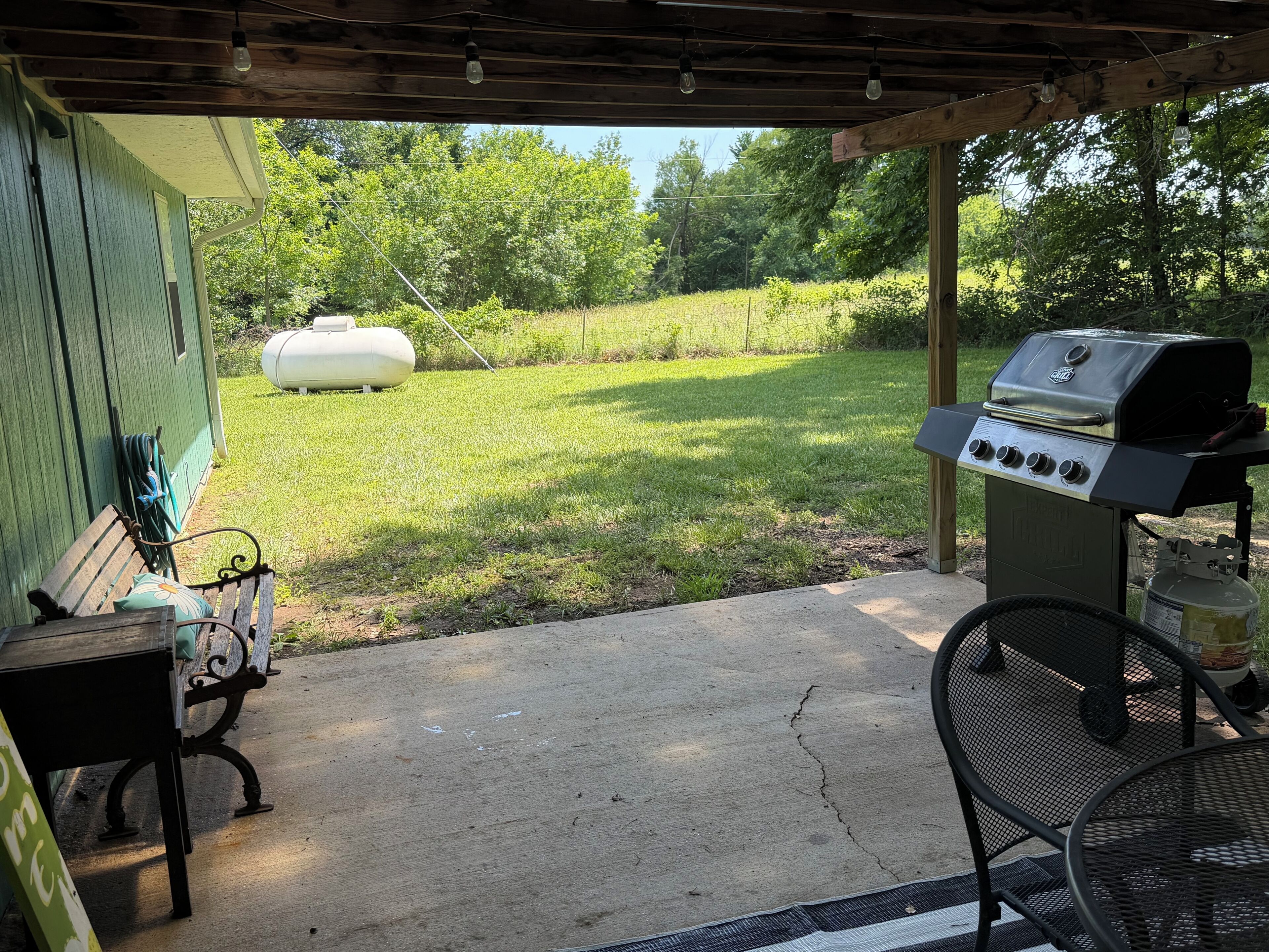 An outdoor patio with a grill, a bench, and a hose reel.