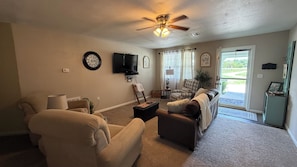 A living room with a ceiling fan, a flat-screen TV, a fireplace, and a view of the outdoors. - Cozy 2 Bedroom Country Cottage North of Parsons . Sleeps up to 5 people. (Parsons)