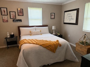 Une chambre à coucher comprenant un lit, des tables de chevet, une commode, une fenêtre avec des stores et des éléments de décoration murale.