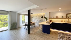 A modern kitchen with a stone accent wall, a dining area with a large table, and a view of greenery through the windows.