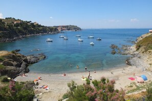 A coastal beach with boats, rocky terrain, and people sunbathing.