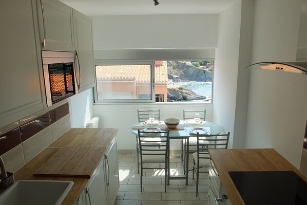A compact kitchen with a view of the ocean, a dining table set with glassware, and a modern light fixture.