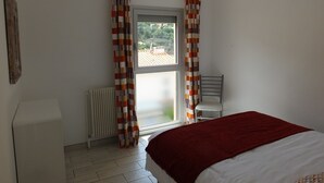 Quarto com cama, ventilador de teto, radiador e janela com cortinas.