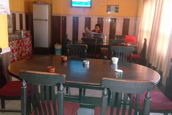 A dining area with a round table, chairs, and a person reading a newspaper.