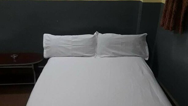 Una cama individual con ropa de cama blanca en una habitación con paredes oscuras.