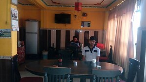 Un comedor con una gran mesa redonda y sillas, un televisor montado en la pared y un refrigerador al fondo.