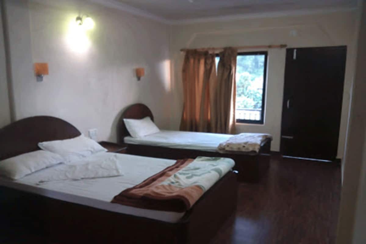 Quarto com duas camas de solteiro, janela com cortinas, porta e luminária fixada na parede.
