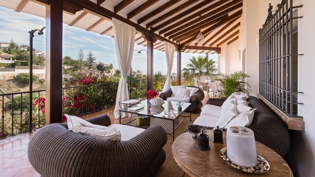 A covered outdoor seating area with wicker furniture, a glass table, and a view of the surrounding landscape. - Luxury Mediterranean Villa, High Standing , Sea Views (Málaga)
