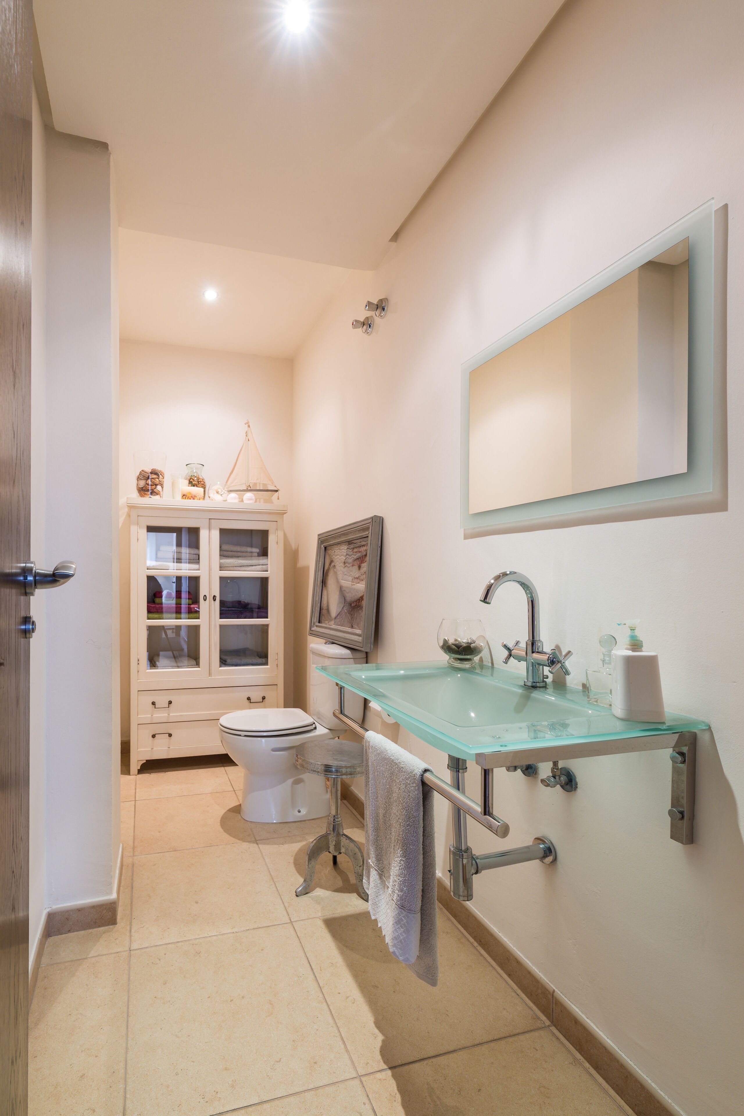 A bathroom with a glass sink, a toilet, a cabinet with glass doors, and a mirror on the wall.