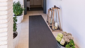 A narrow hallway with white brick walls, a black mat, potted plants, and a wooden bench. - Luxury Mediterranean Villa, High Standing , Sea Views (Málaga)