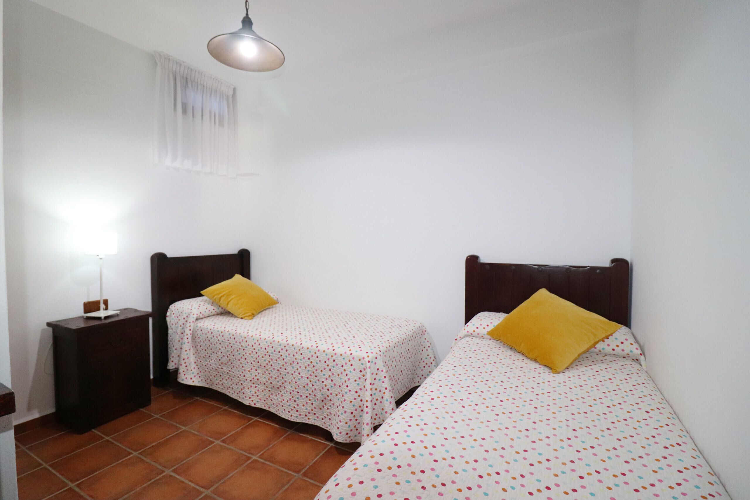 Ein Schlafzimmer mit zwei Einzelbetten, jeweils mit einem gelben Kissen, einem Nachttisch und einer Lampe.